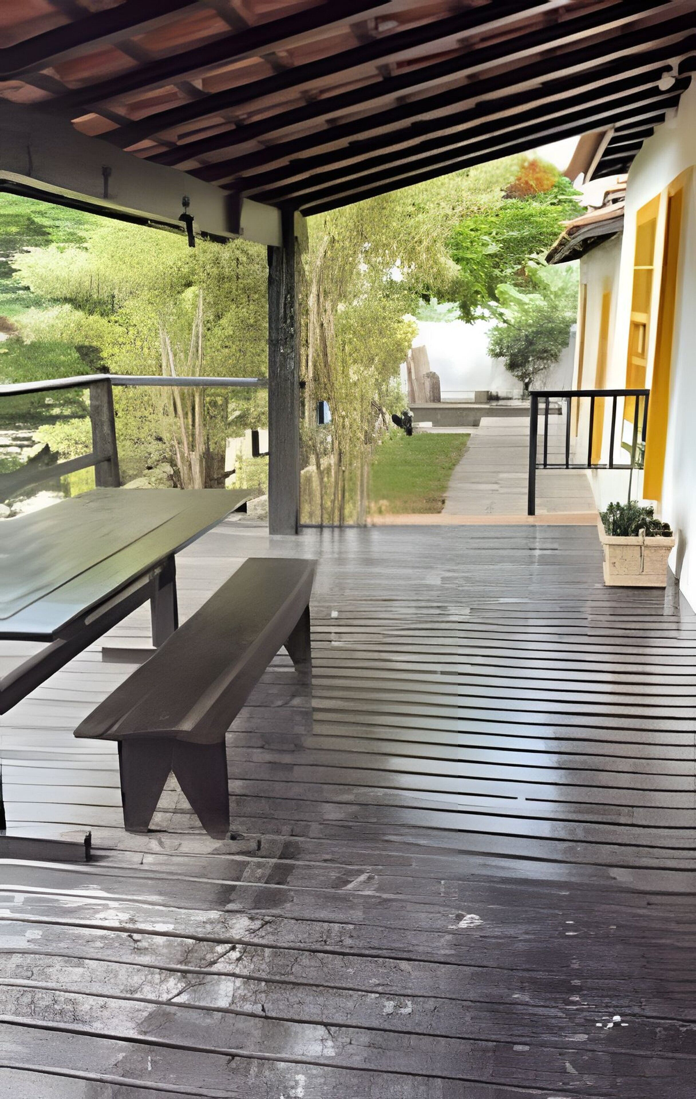 A covered outdoor area with a bench, a potted plant, and a pathway leading to a building.