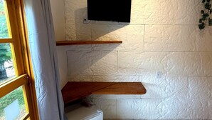 Habitació amb una paret blanca amb textura, una estant de fusta, un televisor de pantalla plana muntat a la part superior i una finestra amb cortines.