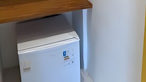Un frigorífic blanc amb un compartiment congelador, una prateleira de fusta i un mirall fixat a la paret.