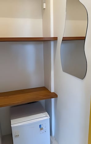 Ein weißer Kühlschrank mit Gefrierfach, einem Holzregal und einem an der Wand befestigten Spiegel.