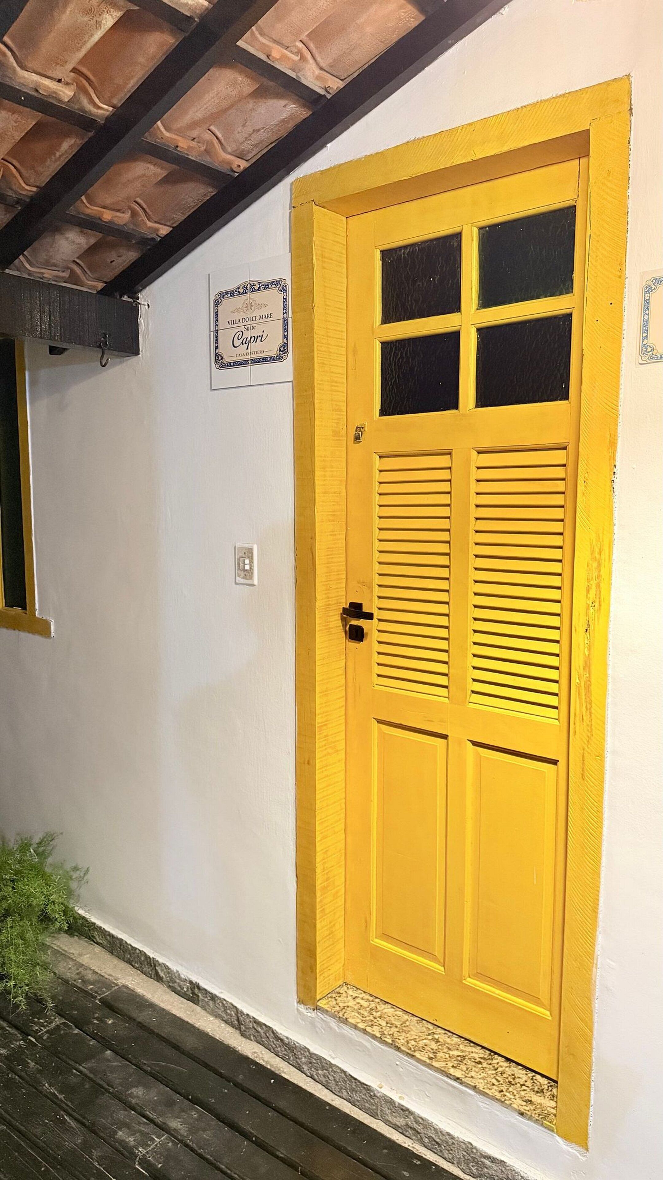 Une porte jaune avec des volets, une enseigne au-dessus, et une petite fenêtre sur le côté gauche.