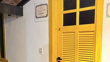 Une porte jaune avec des volets, une enseigne au-dessus, et une petite fenêtre sur le côté gauche.