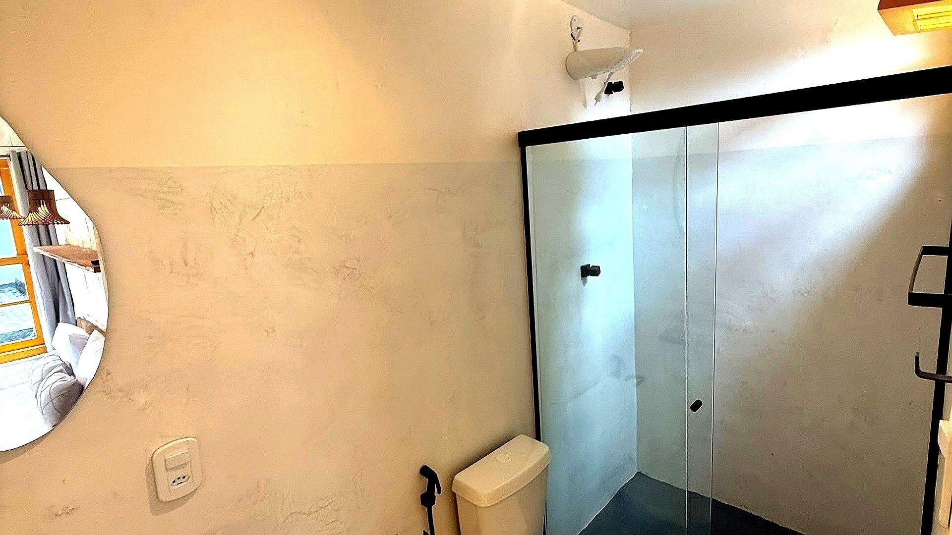 Casa de banho com divisória de chuveiro em vidro, porta-toalhas e interruptor de luz na parede.