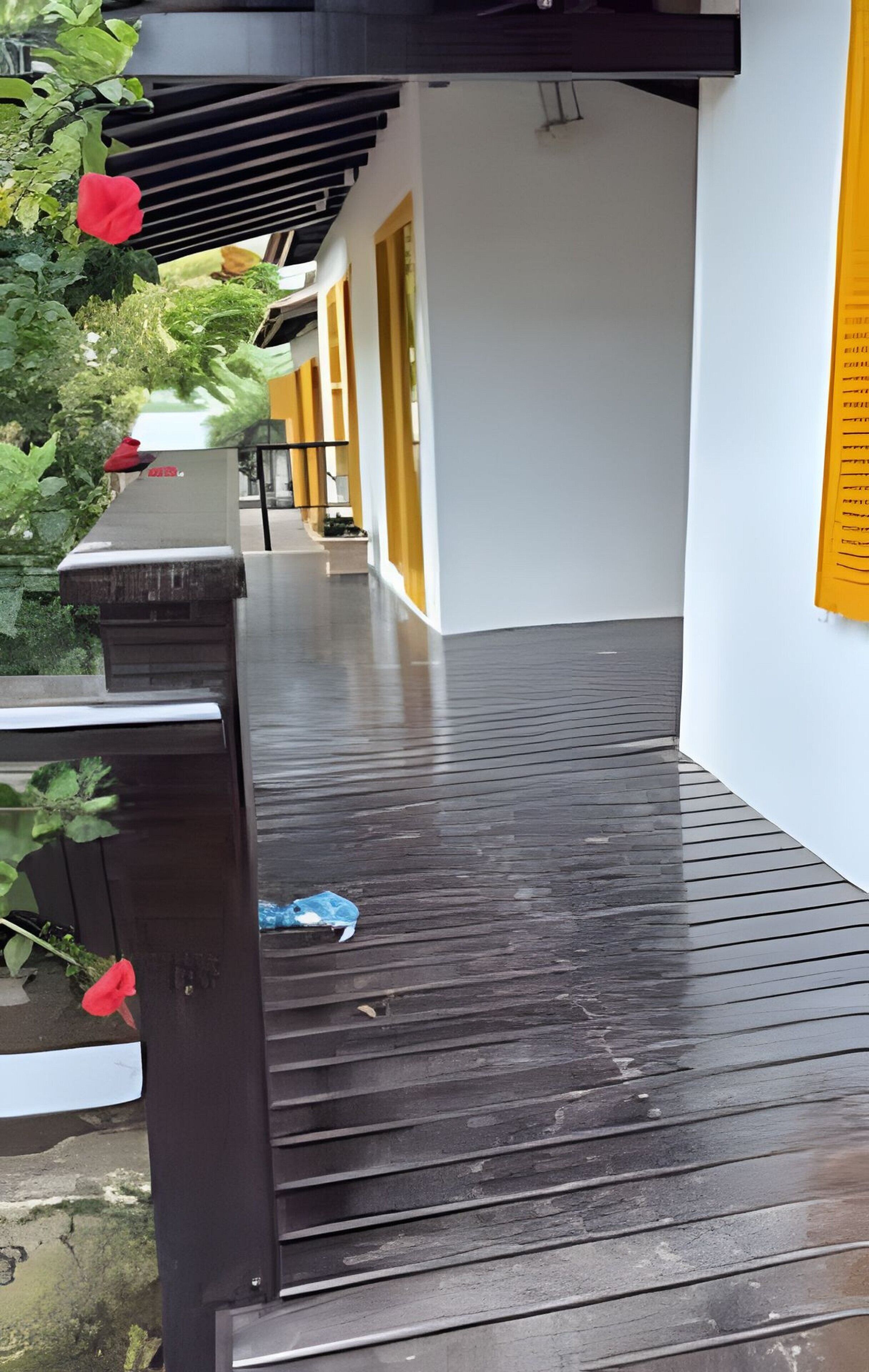 Un espace extérieur abrité doté d’une terrasse en bois, d’un mur blanc orné d’une enseigne jaune et d’une fleur rouge.