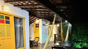 Un porxo exterior cobert amb un hamaca, mobles de fusta i una porta groga.