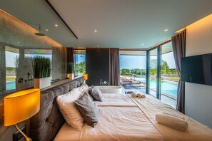 Ein modernes Schlafzimmer mit einem großen Bett, einer Badewanne und Blick auf einen Swimmingpool.