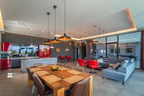 Eine moderne Küche mit einem roten Kühlschrank, ein Essbereich mit einem Holztisch und Stühlen sowie ein Wohnzimmer mit einem grauen Sofa und roten Sesseln.