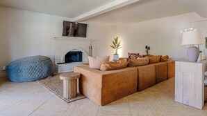 A living room with a sectional sofa, a blue bean bag, a fireplace, and a side table with a lamp.