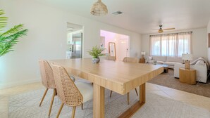 A spacious living area with a wooden dining table, wicker chairs, a sofa, and a ceiling fan.