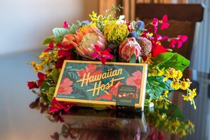 A box of Hawaiian Host Island Mac's chocolates on a table with a floral arrangement. - Honua Kai 4 Free Rental Cars KBM Resorts Gorgeous Inner Courtyard 4 Units, 7 Bedrooms HK Ml-2731 (Kaanapali)