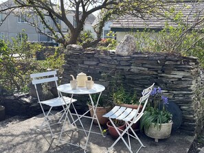 A stone wall, a round table with chairs, a teapot, and cups. - Sunnybrae Cottage (Tintagel)