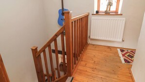A wooden staircase with a blue guitar leaning against the wall, a radiator, and a small window with a statue. - The Ranch (Prestatyn)