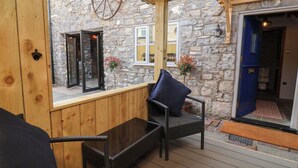 A wooden deck with wicker furniture, stone walls, and a large window. - The Ranch (Prestatyn)