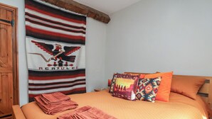 A bed with a red blanket, a patterned pillow, and a blanket with a horse and rider design. - The Ranch (Prestatyn)
