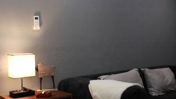 Een kamer met een bed, een nachtkastje met een lamp, een klein tafeltje en een donkergroene bank met kussens.