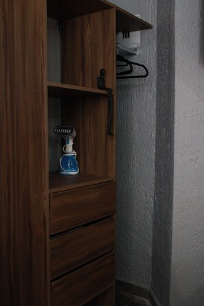 Un armari de fusta amb un aparell blau, possiblement una cafetera, i una perca negra penjada a la paret.
