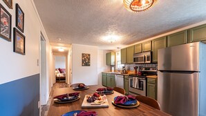 Une cuisine moderne avec des meubles verts, des appareils en acier inoxydable et un coin repas agrémenté d’une table en bois dressée pour le repas.