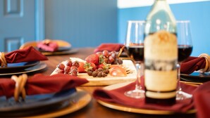 Une table à manger avec une bouteille de vin, des verres et une variété de fruits et de pâtisseries.