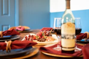 Une table à manger avec une bouteille de vin, des verres et une variété de fruits et de pâtisseries.