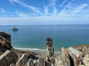 A coastal landscape with a prominent rock formation in the foreground, a distant island, and a clear blue sky. - The Hideaway (Tintagel)