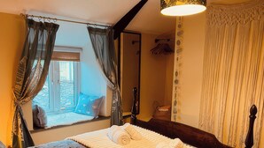 A bedroom with a bed, a window with curtains, a mirror, and a wall with a decorative pattern. - The Hideaway (Tintagel)