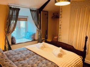 A bedroom with a bed, a window with curtains, a mirror, and a wall with a decorative pattern. - The Hideaway (Tintagel)