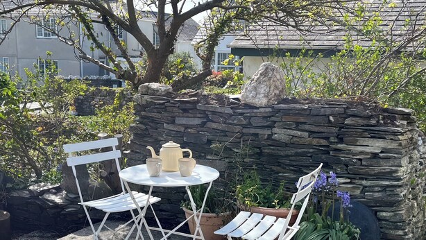 A stone wall, a white metal table with chairs, and a teapot set. - The Hideaway (Tintagel)