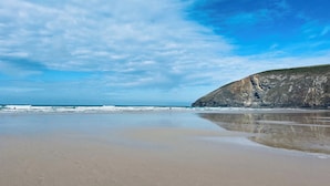 A beach with a clear sky, calm sea, and a rocky cliff. - The Hideaway (Tintagel)