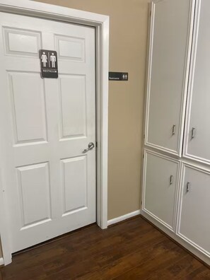 A white door with a restroom sign, a beige wall, and a set of white cabinets. - Lofty Grace Home 2 (Richmond)