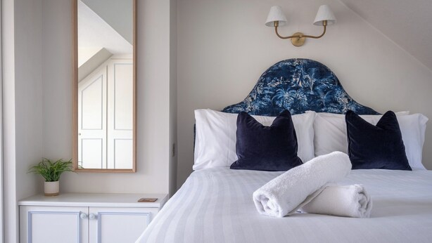 A neatly made bed with white linens and a rolled towel, a dark blue headboard, and a wall-mounted light fixture. - Marina View (Windermere)