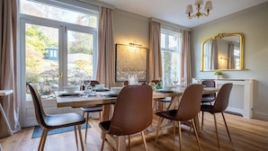 A dining area with a table set for four, wooden chairs, a chandelier, and a large window with curtains. - Marina View (Windermere)