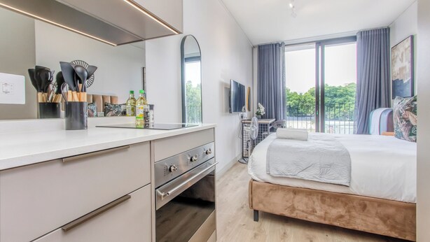 Une chambre d’hôtel moderne dotée d’une kitchenette, d’un grand lit, d’une télévision et d’un balcon avec vue.