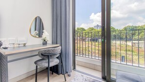 Une chambre moderne équipée d’un bureau, d’une chaise et d’une grande fenêtre offrant une vue sur la verdure et les bâtiments.