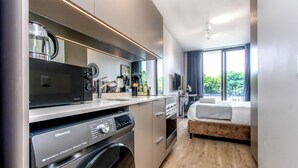 Une chambre d’hôtel moderne équipée d’un coin cuisine, d’un lave-linge, d’un lit et d’une grande fenêtre.
