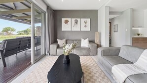 Ein modernes Wohnzimmer mit einem grauen Sofa, einem schwarzen Couchtisch mit einer Vase und einer Glastür, die zu einem Außenbereich führt.