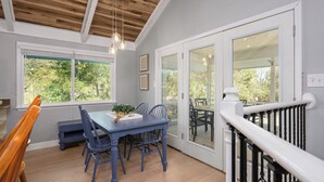 A dining area with a blue table and chairs, a wooden bench, and a view through large glass doors to an outdoor patio. - Ocean Sound - 2nd Row - 4BR Folly Field Beach House - Heated Private Pool (Hilton Head Island)