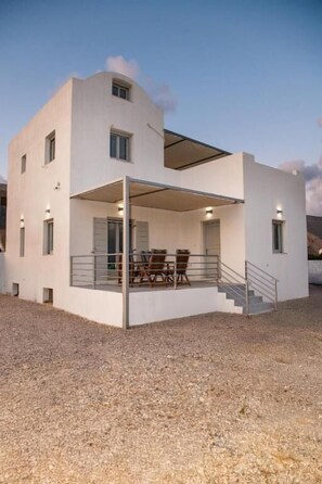 Una casa moderna de dos pisos con un porche cubierto, una escalera y un camino de entrada de grava.