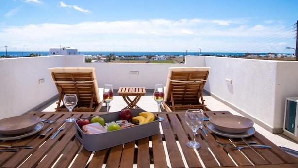 Una terraza con dos sillas de madera, una mesa y un frutero.