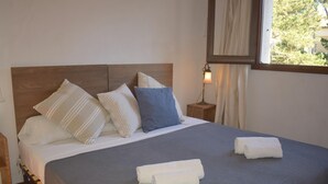 Cama bem arrumada com almofadas e toalhas, cabeceira de madeira, abajur e janela com cortinas.