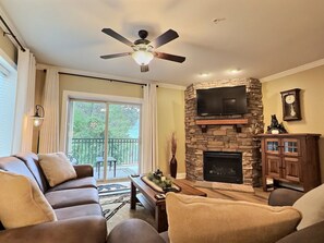 A living room with a stone fireplace, a ceiling fan, a sofa, and a television mounted on a stone wall.