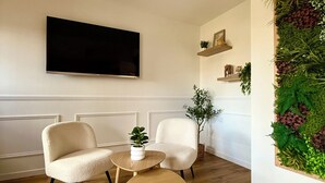 Una sala de estar con televisor de pantalla plana, dos sillones, una mesita, alfombra tejida y un jardín vertical.