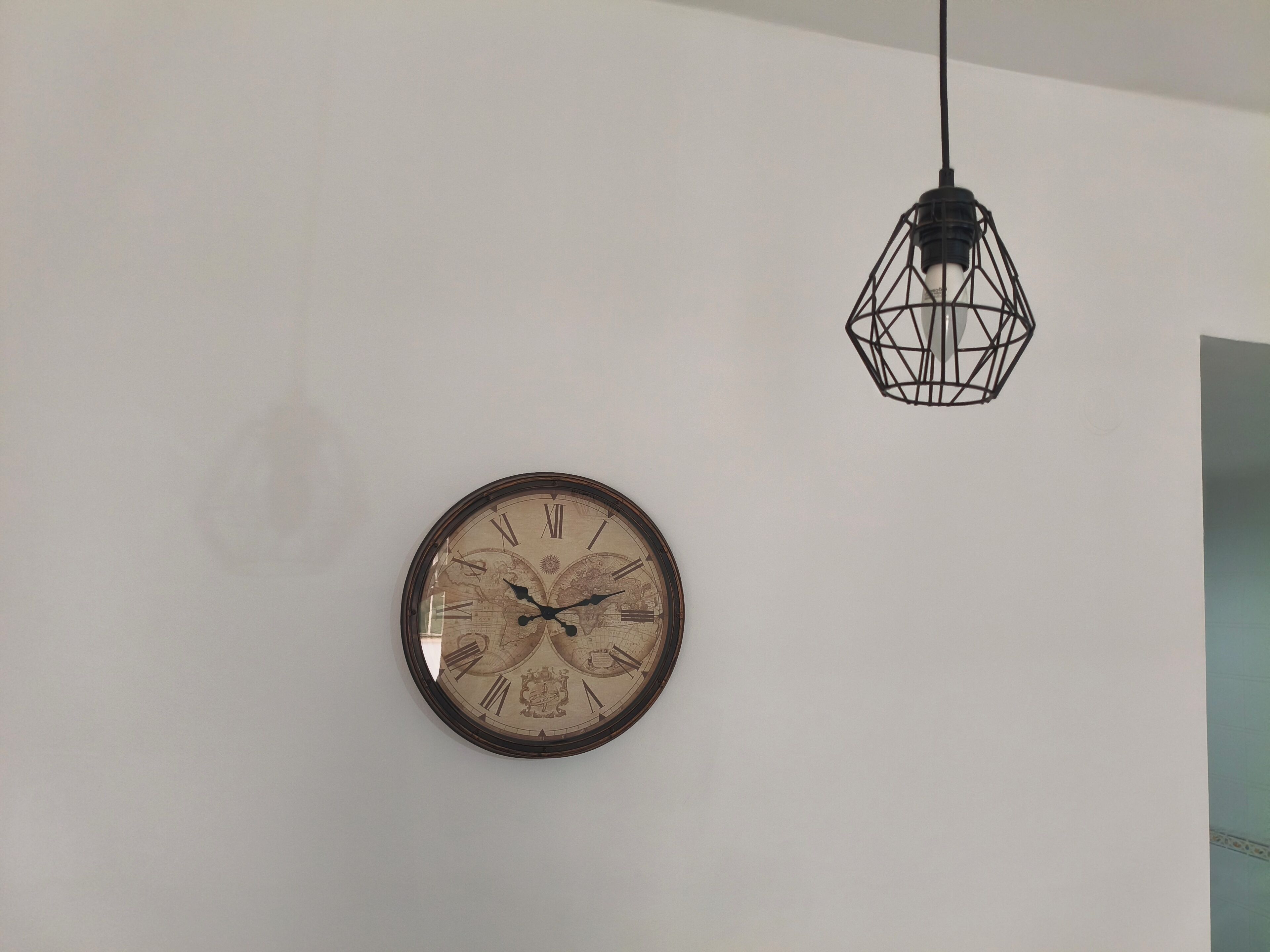 Een wandklok met Romeinse cijfers en een decoratief ontwerp, en een hangende geometrische lamp.
