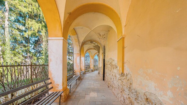 Un couloir orné d’arches, doté de bancs et recouvert d’un sol en pierre.