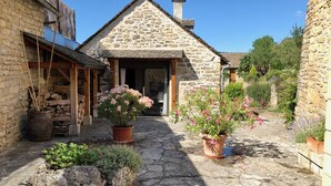 A stone building with a tiled roof, a wooden porch, and potted plants. - La grande du Bruel - ESCLANEDES (ESCLANEDES)