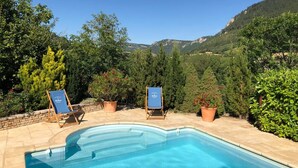 A swimming pool with two lounge chairs, surrounded by potted plants and trees, with a mountainous backdrop. - La grande du Bruel - ESCLANEDES (ESCLANEDES)
