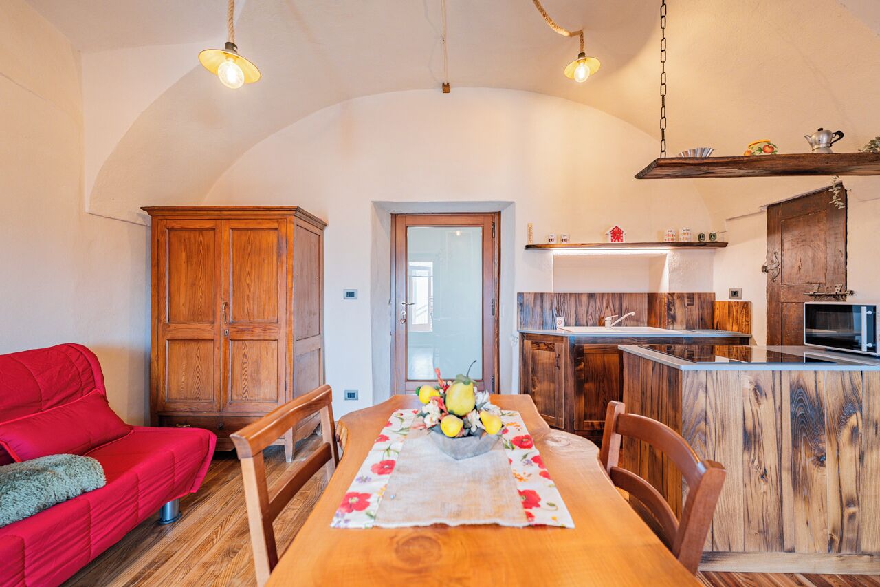 Una cucina accogliente con mobili in legno, un tavolo da pranzo con tovaglia floreale e un divano rosso.