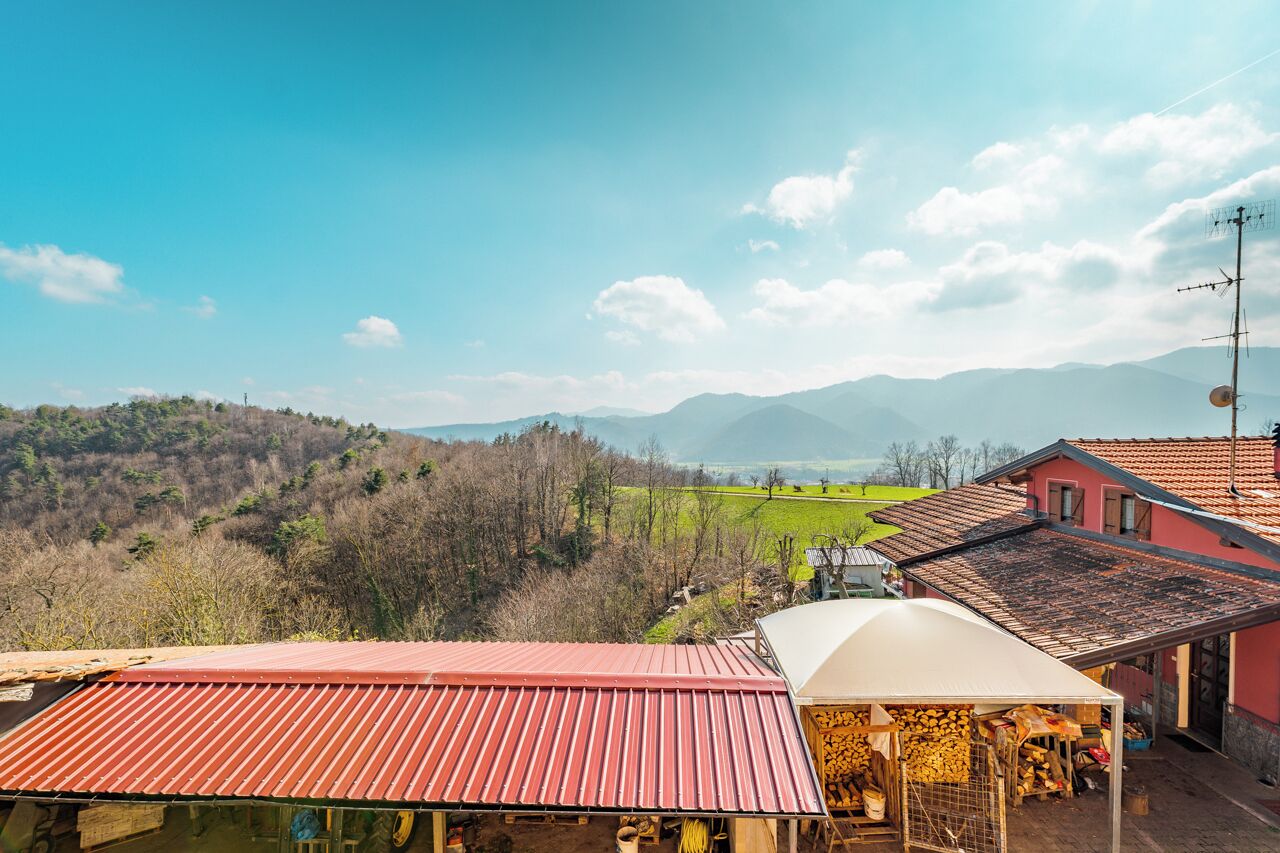 A rural setting with a house featuring a red roof, a covered porch, and a view of green fields and mountains.