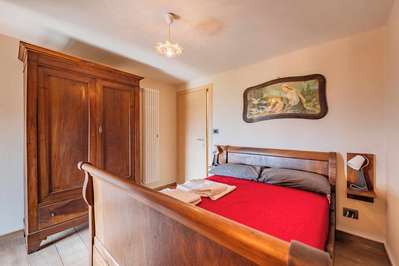 Een slaapkamer met een houten bed, een rode sprei, een houten garderobe, een radiator en een schilderij aan de muur.