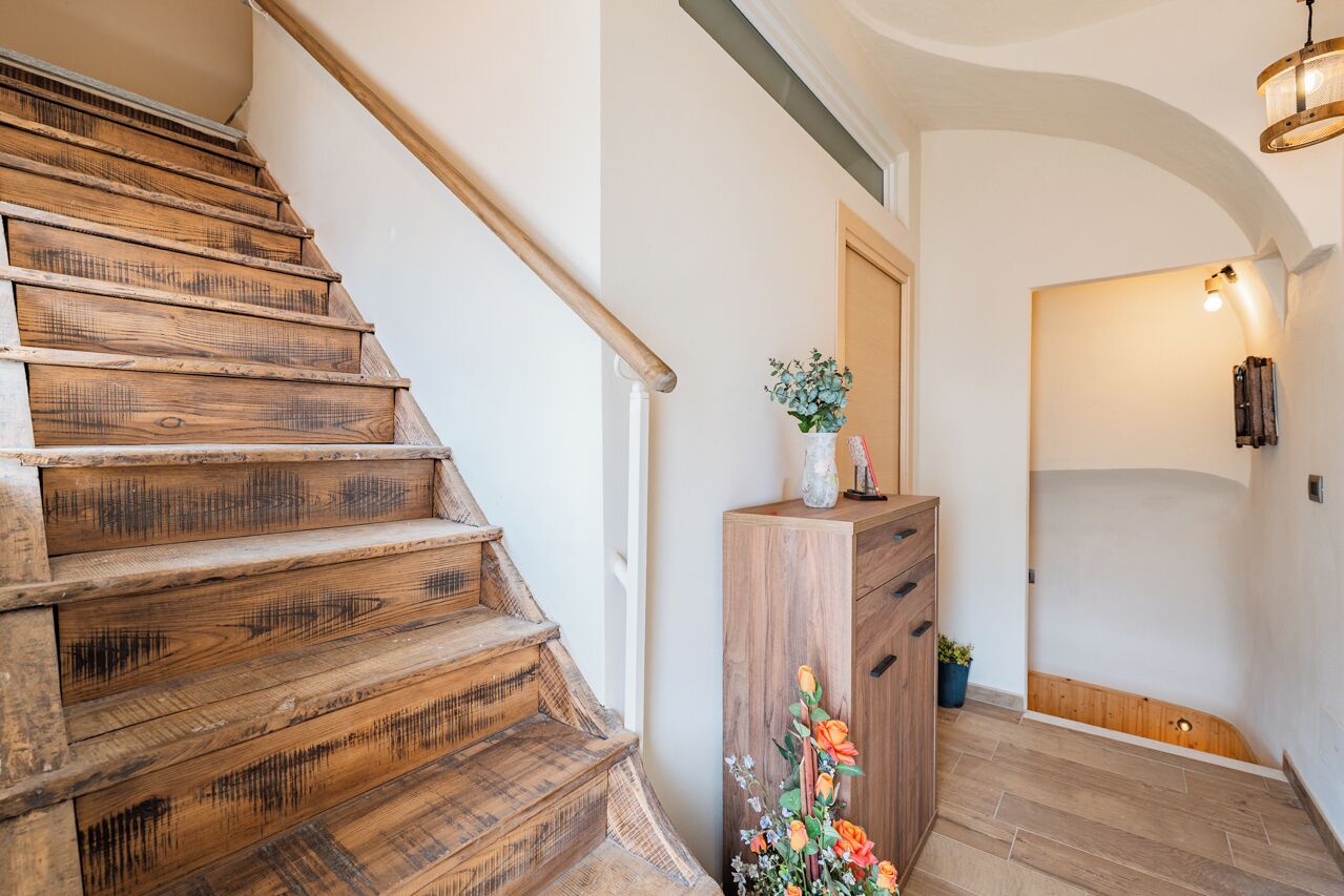 Een houten trap die uitkomt op een plateau met een houten kast en een bloevas.