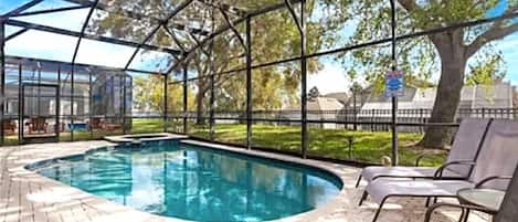 An indoor swimming pool with a glass enclosure, surrounded by brick flooring and metal chairs.